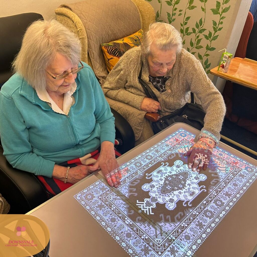 Two elderly women using an interactive table, exploring a colorful patterned display together.