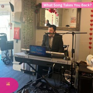 Man singing and playing a keyboard in a care home room decorated with heart ornaments.