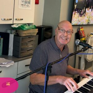 Man smiling while playing a keyboard and singing into a microphone in a room.
