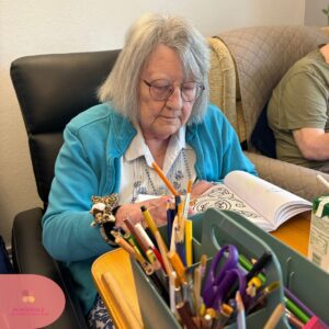 Elderly woman coloring a picture with pencils at a table.