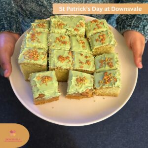 Plate of green frosted cake squares with sprinkles being held by someone.