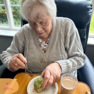 Elderly woman eating a piece of green cake with a spoon.