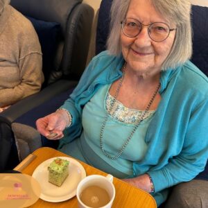 Smiling elderly woman with tea and cake at a table.