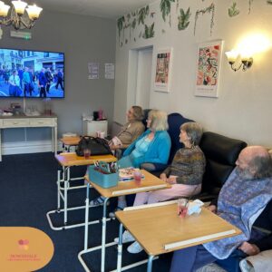 Elderly residents sitting together watching TV in a lounge.