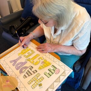 Elderly woman sitting in a chair, colouring an Easter-themed activity sheet.