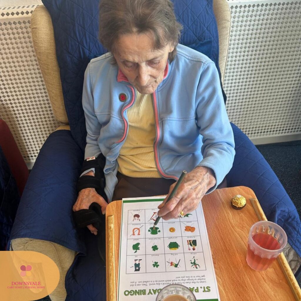 Elderly woman completing a St. Patrick’s Day bingo activity at a table.