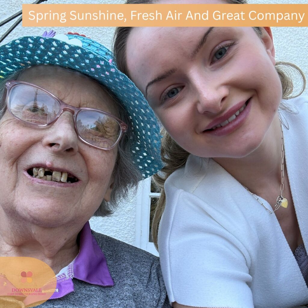 Close-up selfie of a young woman and an elderly woman wearing a hat, both smiling outdoors.