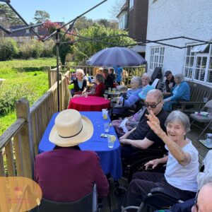 Group of older adults gathered around tables on a sunny patio, chatting and enjoying drinks.