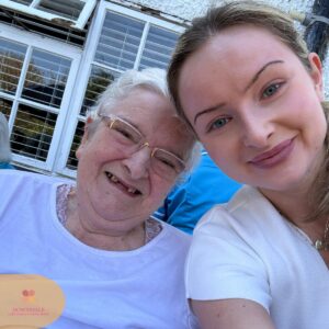 Close-up selfie of a young woman and an elderly woman smiling together outdoors.