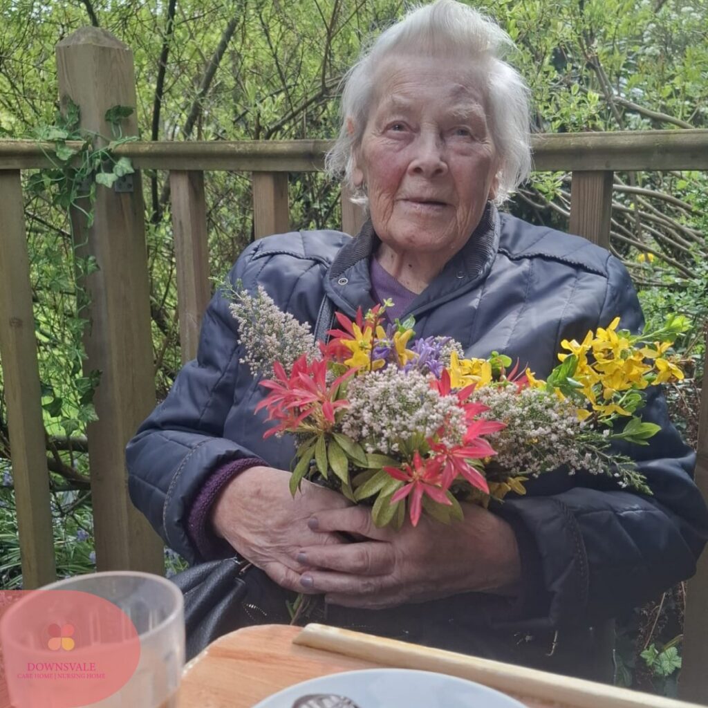 Elderly woman sitting outdoors holding a colorful bouquet of flowers.