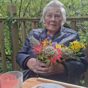 Elderly woman sitting outdoors holding a colorful bouquet of flowers.