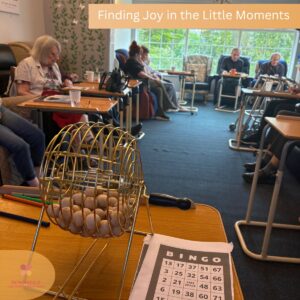 Care home residents gathered for a bingo activity with a bingo cage and cards in the foreground.