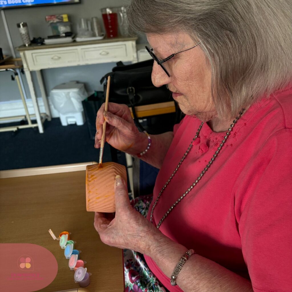 Elderly woman adding paint to a textured clay pot.