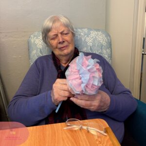 Elderly woman holding a pink and blue tissue paper flower.