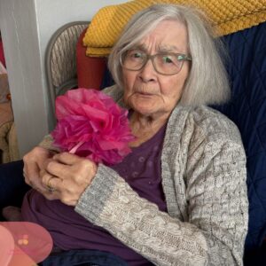 Elderly woman holding a bright pink paper flower.