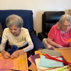 Two elderly women crafting with colorful paper and pipe cleaners.