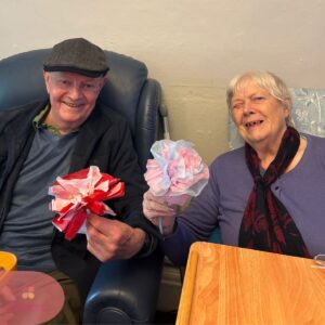 Elderly couple smiling and showing their finished paper flowers.
