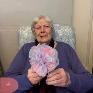 Elderly woman holding a pink and blue paper flower.
