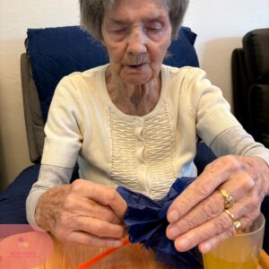 Elderly woman carefully folding blue tissue paper at a table.