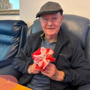Elderly man smiling while holding a red and white paper flower.