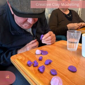 An elderly man creating shapes with purple clay at a table during a creative clay modelling activity.