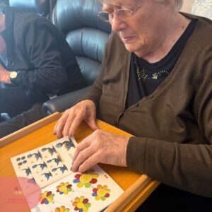 Elderly woman doing a colourful activity book exercise at a table.

