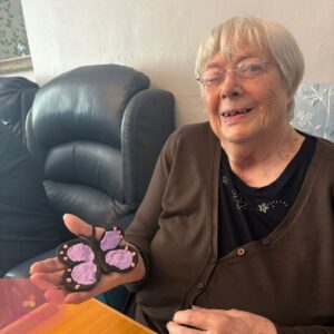 Elderly woman smiling while holding a handmade butterfly craft.