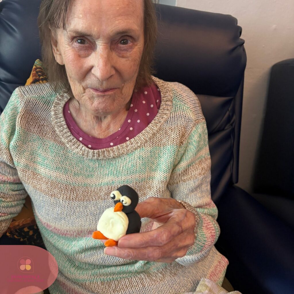 Senior woman sitting comfortably and showing a handmade penguin decoration.