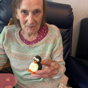 Senior woman sitting comfortably and showing a handmade penguin decoration.