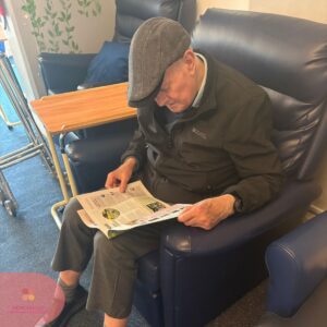 Elderly man relaxing in an armchair while reading a newspaper in a nursing home.