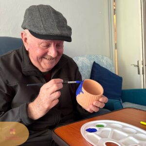 Elderly resident painting a small clay pot during an arts and crafts session.