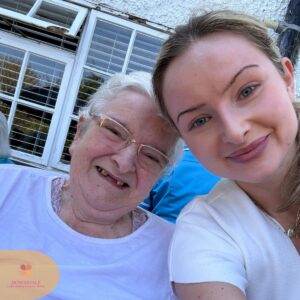 Elderly resident and young woman smiling together for a selfie outdoors.
