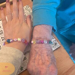 Two hands wearing matching colourful handmade bead bracelets.
