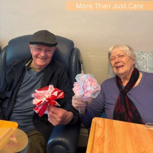 Two care home residents proudly holding handmade tissue paper flowers.