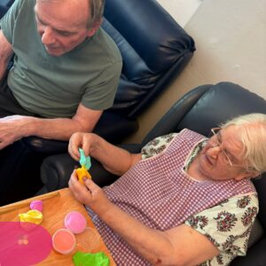 Two seniors sitting together, creating colorful clay shapes at a table.
