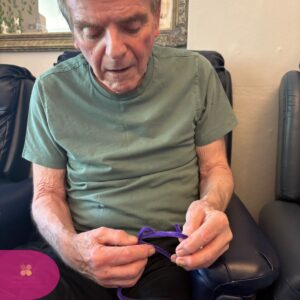 Elderly man concentrating while bending a purple pipe cleaner.