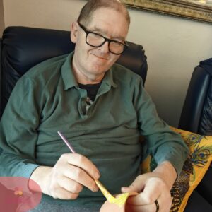 Smiling resident painting a craft project while seated in a care home lounge.