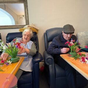 Two care home residents creating colourful flower arrangements during a group activity.