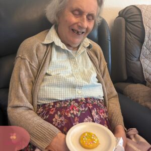 Elderly woman smiling while holding a decorated biscuit during a care home activity.