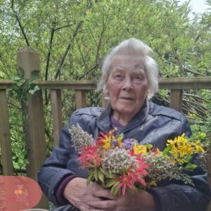 Elderly woman holding a colorful bouquet in a garden.