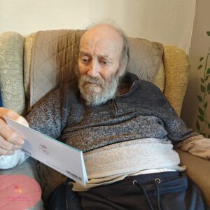 Resident seated in an armchair, carefully reading a greeting card.