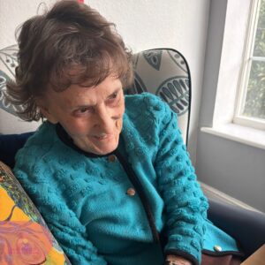 Elderly female resident smiling while sitting comfortably in a chair by the window at Downsvale Care Home.