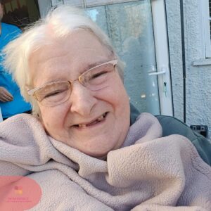 Smiling resident wrapped in a soft blanket, enjoying time outdoors in the sunshine.