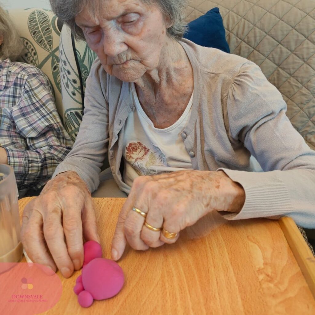 Elderly resident carefully shaping pink modelling clay during an afternoon activity.