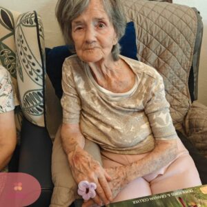 Elderly resident holding a handmade flower craft while seated comfortably.