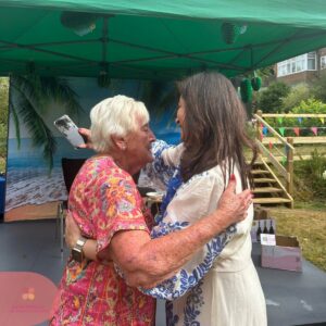 Two women share a warm embrace at an outdoor care home event.