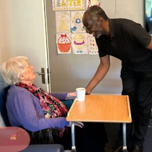 Caregiver warmly serves a drink to a resident in a care home.