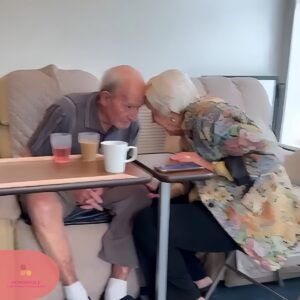 An elderly couple sit closely together sharing a quiet moment.