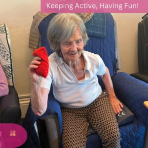 Smiling resident raising a bean bag during an engaging seated activity session.