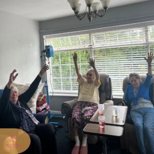 Residents enjoying a seated group exercise session with raised arms.